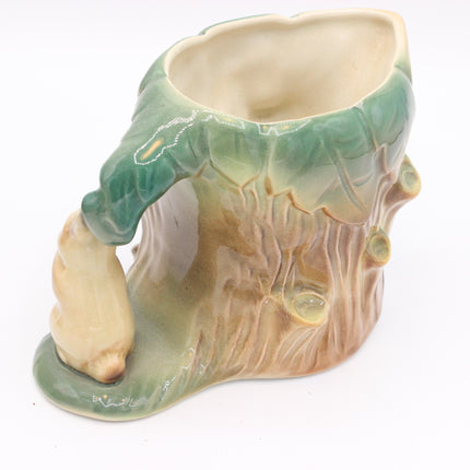 A ceramic mug shaped like a tree stump with a green leafy rim and a small bear figurine attached to the side, shown on a plain white background.