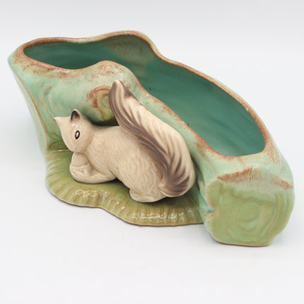A ceramic planter shaped like a tree trunk with a sculpted squirrel figure in front, featuring a glossy light green glaze and brown accents, photographed on a white background.