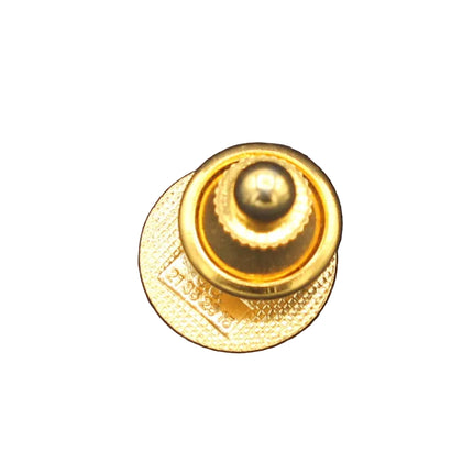 A small gold metal button or pin with a round top and textured circular base, placed on a dark navy blue textured fabric background.