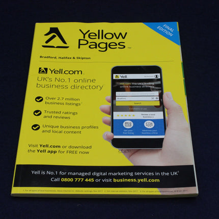 Yellow Pages book with a smartphone displaying Yell.com on a dark background