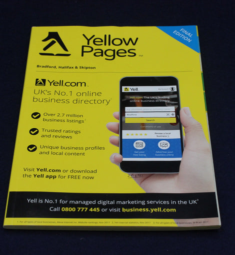 Yellow Pages book with a smartphone displaying Yell.com on a dark background