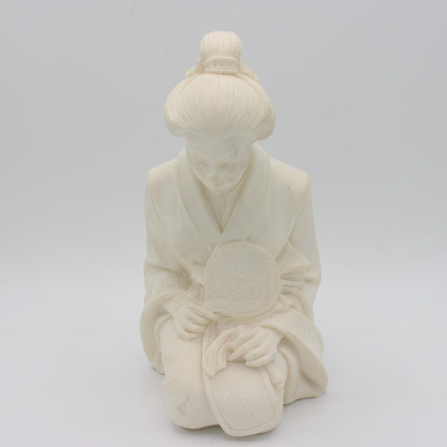An off-white a alabaster figurine of a kneeling figure in traditional robes holding a round fan, set against a seamless light gray background. 