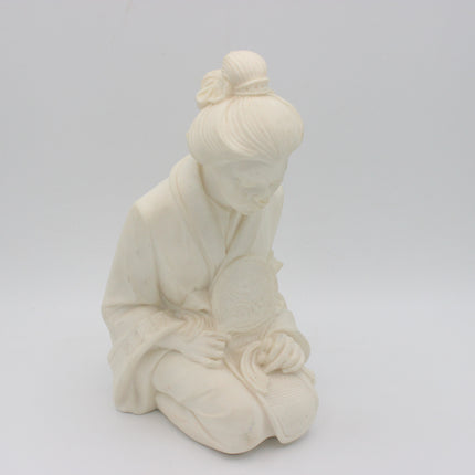 An off-white alabaster  figurine of a kneeling woman in traditional robes holding a folding fan, set against a seamless light gray background.