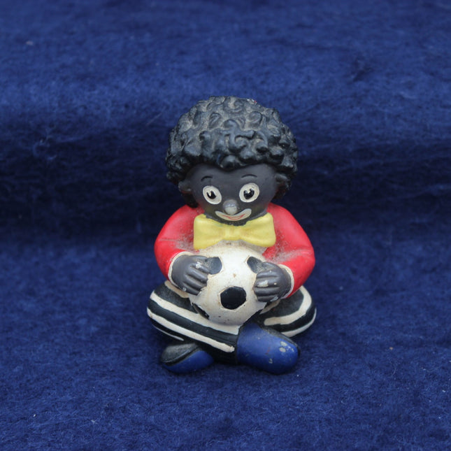 Figurine of a Golly holding a soccer ball on a blue fabric background