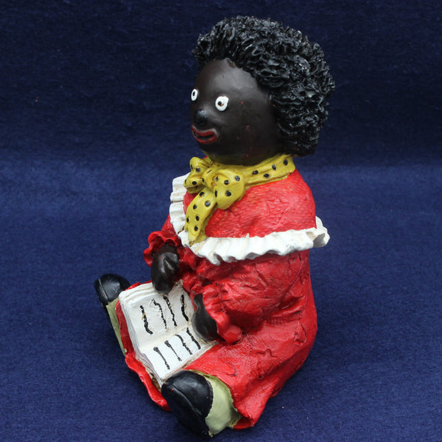 Figurine of a Golly in red attire with a yellow scarf on a blue background