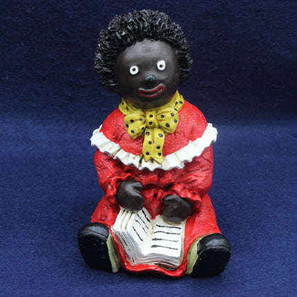 Figurine of a Golly in red dress with a yellow bow and black hair on a blue background