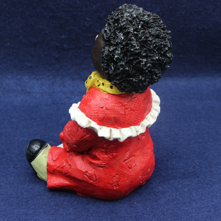 Figurine of a Golly wearing a red outfit with a black afro on a blue background