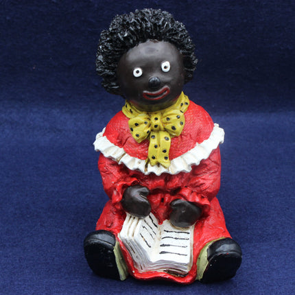 Figurine of a Golly in red with a yellow bow and black hair on a blue background