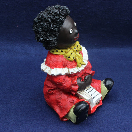 Golly Figurine in a red dress with a yellow bow, sitting on a blue background