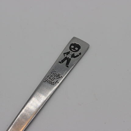 A close-up of a silver metal spoon handle engraved with a Golly and slogan Golly It's Good