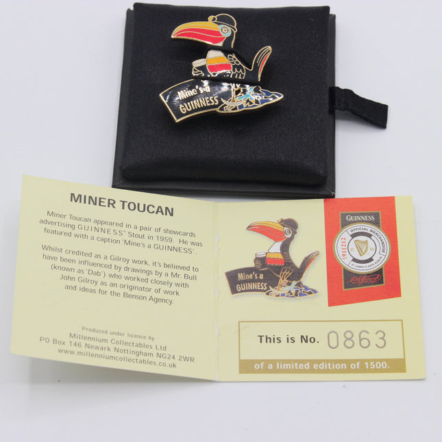 A Guinness Miner Toucan enamel pin displayed with its black fabric pouch and an accompanying paper certificate insert on a white background.