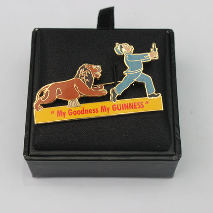 Enamel pin with a lion and person design and 'My Goodness My GUINNESS' text on a black box.