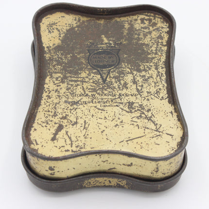 A vintage metal tin with a distressed cream-colored enamel top and dark brown rusted edges, featuring an embossed 'Made in England' shield logo in the center.