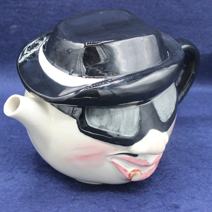Teapot shaped like a face with a black hat on a blue background