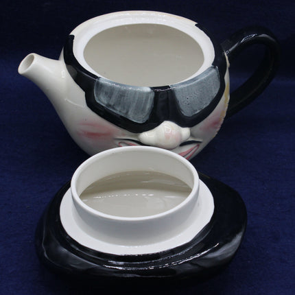 Ceramic teapot and cup with face design on a dark blue background