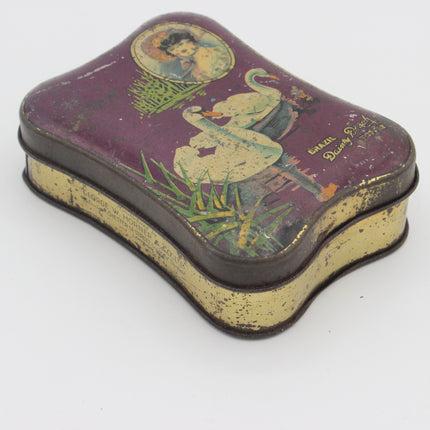 Vintage tin box with a purple lid featuring a painted illustration of a woman and a snake, with a distressed gold-toned base and rim, photographed on a white background.