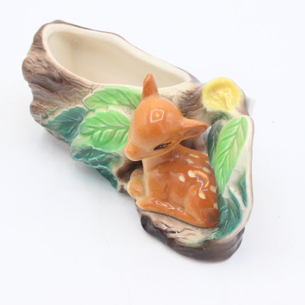 A ceramic woodland-themed flower pot shaped like a tree trunk with a glossy orange-brown deer figurine sitting among green leaves and a yellow flower on a white background.