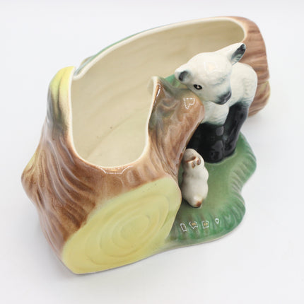 A ceramic planter shaped like a tree stump with painted animal figures, including a white lamb and a black-and-white calf, on a green base against a plain white background.
