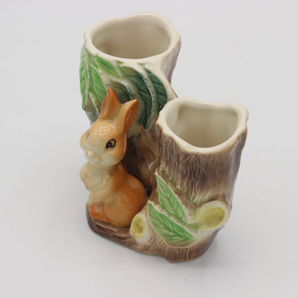 A ceramic two-tiered vase designed to look like tree stumps with green leaves, featuring a small glazed rabbit figurine on the front, set against a plain white background.