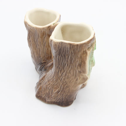 A vase that  looks like tree stumps with realistic bark texture, featuring a light beige glazed interior and a small green leaf detail on the side, set against a plain white background.