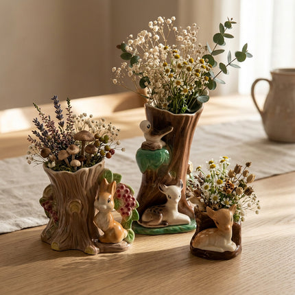 Three ceramic woodland-themed planters shaped like tree stumps with rabbits, deer, and a bird, shown on a kitchen table