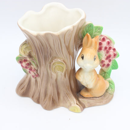 A ceramic tree stump planter with a small beige rabbit figurine, green leaves, and pink berries on a white background.