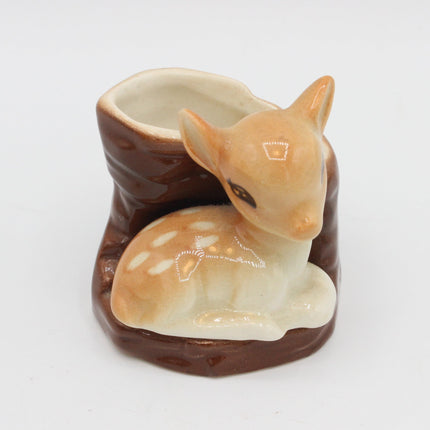A ceramic fawn planter shaped like a reclining deer sitting on a brown faux-wood base, photographed on a plain white background.