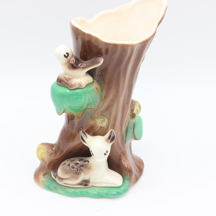 A ceramic tree stump planter with painted woodland animals, including a small bird on a green branch and a white rabbit nestled at the base, set against a plain white background.