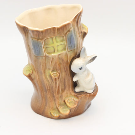 A ceramic tree stump planter with a small white rabbit figurine perched on the side, featuring a glazed finish in earthy brown, beige, and soft green tones.