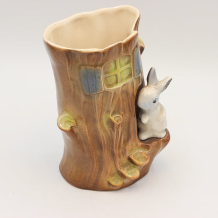 A ceramic tree stump-shaped cup or planter with a small white rabbit figurine on the side, photographed against a plain light gray background.