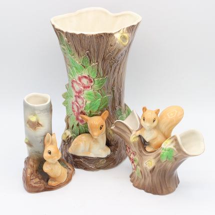 A ceramic woodland-themed set featuring a large tree trunk planter with a deer, a small cylindrical pot, and two squirrel figurines on a light gray background.