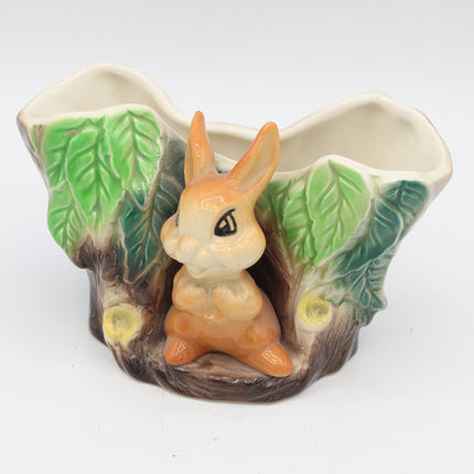 A ceramic planter shaped like a tree trunk with a small orange rabbit figurine in the center, green leafy sides, and two small yellow flower details, photographed on a white background.