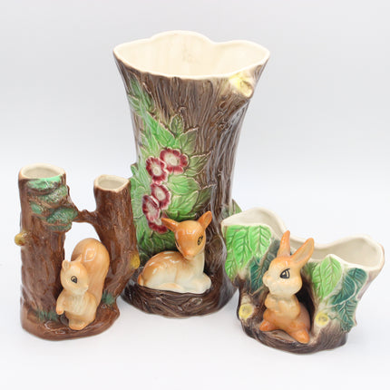 A ceramic woodland-themed tableware set featuring a large tree trunk planter with a deer and flowers, a small tree stump holder with a squirrel, and a rabbit-shaped planter, all on a white background.