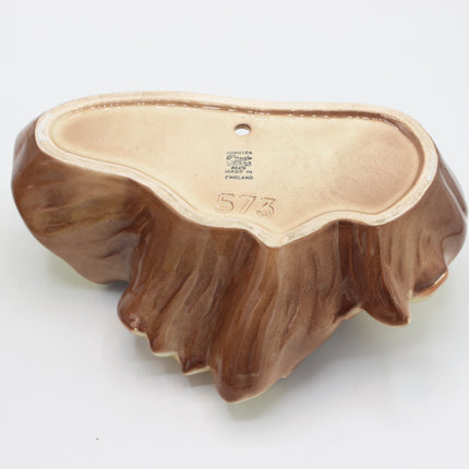 A vintage ceramic wall-mounted planter shaped like a tree trunk, featuring a glossy brown textured exterior and a light beige glazed interior with a small hole for hanging.