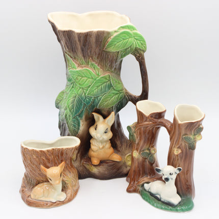 A ceramic woodland-themed pitcher set shaped like tree stumps and trunks, featuring green leaves, animal figures including a rabbit, fox, and lamb, and a cream-colored interior, photographed on a light gray background.