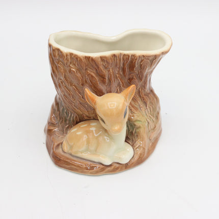 A ceramic planter shaped like a tree stump with a small fawn figurine sitting in front, photographed on a plain white background.