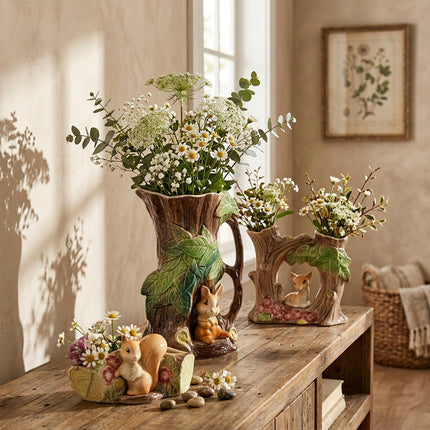 A ceramic woodland animal set shaped like tree stumps and logs, featuring green leaves, brown bark, and small rabbit and squirrel figurines, photographed on a light gray studio background.