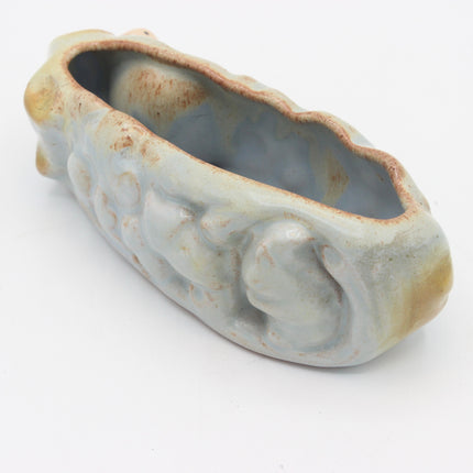 A small carved ceramic planter or vase with a pale blue-gray glaze and warm tan-brown weathered edges, photographed on a plain white background.