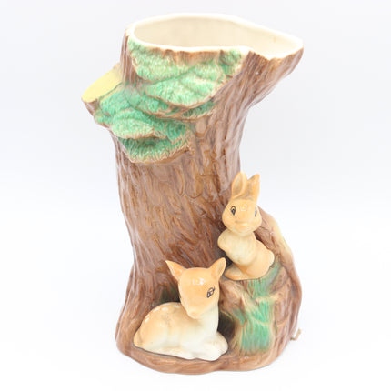 A ceramic tree stump planter featuring two small rabbit figurines and green leafy detailing, set against a plain white background.