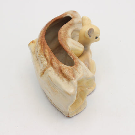 A vintage ceramic birdcage shaped like a tree trunk with a small cream-colored bird figurine perched on top, shown on a plain white background.