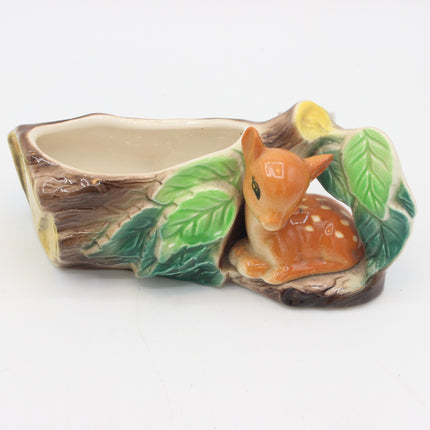 A ceramic woodland-themed planter shaped like a tree stump with a fawn figurine nestled among painted green leaves on a white background.