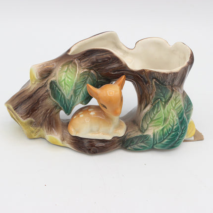 A ceramic woodland-themed planter shaped like a hollow tree trunk with a small white deer nestled inside, featuring green leaves and a cream-colored interior opening, shown on a plain white background.