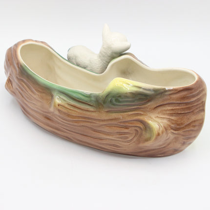 A ceramic planter shaped like a tree trunk with a small white animal figurine on the rim, photographed on a plain white background.