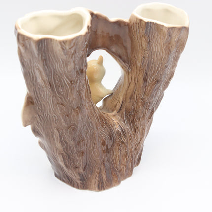 A ceramic double cup or vase designed to look like a tree trunk with bark texture, featuring two open cup-like slots at the top and a small carved animal figure in the center, shown on a white background.