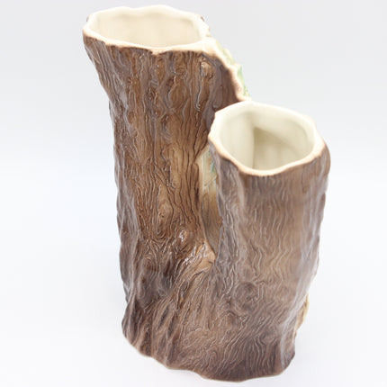 A ceramic double-vase shaped like tree stumps, featuring a textured brown bark exterior and a glossy cream-colored interior, set against a plain white background.