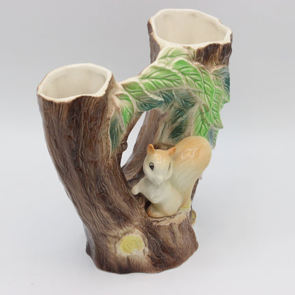 A ceramic double cup holder designed as a tree stump with a small squirrel figurine and green leaves, photographed against a neutral light gray background.
