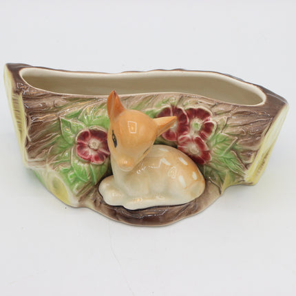 A ceramic planter shaped like a tree trunk with a small fawn figurine sitting in front, decorated with painted flowers and green leaves, on a white background.