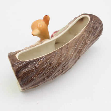 A ceramic planter shaped like a tree trunk with a small deer figurine peeking out from the top, photographed on a plain white background.