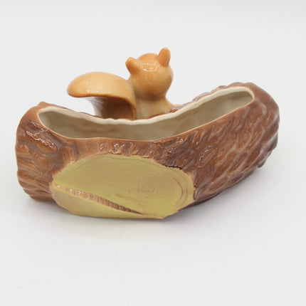 A ceramic squirrel-shaped dish or planter shaped like a log, with a small tan squirrel figure emerging from an open log-shaped cavity, photographed on a plain white background.