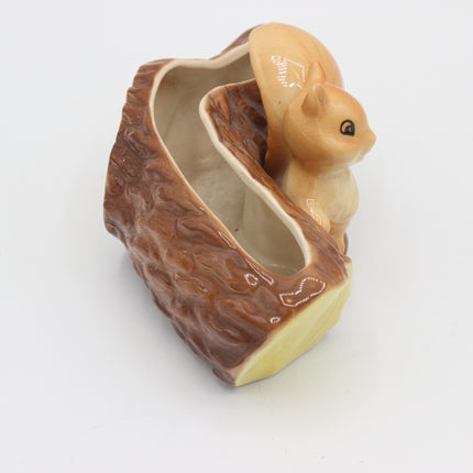 A ceramic squirrel figurine perched on a log-shaped container, shown on a plain white background.